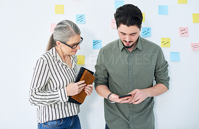 Buy stock photo Shot of two businesspeople using a cellphone together in an office