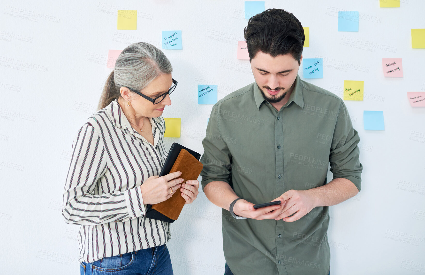 Buy stock photo Shot of two businesspeople using a cellphone together in an office