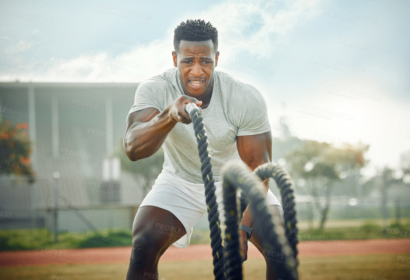 Buy stock photo Cropped shot of a handsome young male athlete exercising with battle ropes outside