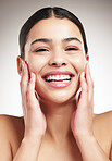 Portrait of a young joyful beautiful mixed race woman touching and feeling her face posing against a grey studio background. Confident hispanic female smiling while posing against a background