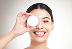 Portrait of a young happy mixed race woman holding a lotion jar while standing against a grey studio background alone. One cheerful hispanic female applying cream to her body while standing against a background