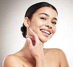 Portrait of a young beautiful mixed race woman touching and feeling her face posing against a grey studio background. Confident hispanic female posing against a background