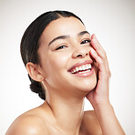 Portrait of a young cheerful beautiful mixed race woman touching and feeling her face posing against a grey studio background. Confident hispanic female smiling while posing against a background