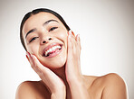 Portrait of a young joyful mixed race woman touching and feeling her face posing against a grey studio background. Confident hispanic female smiling while posing against a background