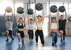 Diverse group of active young people doing overhead medicine ball lunge exercises while training together in a gym. Focused athletes challenging themselves by holding weighted equipment to build muscle and endurance during a workout in a fitness class