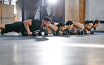 Diverse group of active young people doing push up exercises with dumbbells while training together in a gym. Focused athletes doing press ups with heavy weights to build muscle and endurance during a workout in a fitness class