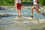 Two friends walking over rocks crossing a river during a hiking trip. Women on holiday on a hiking trip together crossing a river