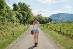 Woman traveling alone taking photos using her digital camera while standing in the road. Young woman on holiday alone taking photos with her digital camera next to a vineyard in the countryside