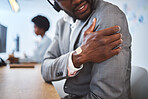 Closeup of one stressed african american businessman suffering with arm and shoulder pain in an office. Entrepreneur rubbing muscles and body while feeling tense strain, discomfort and hurt from bad sitting posture and long working hours at desk