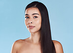 Portrait of one beautiful young hispanic woman with healthy skin and sleek long hair posing against a blue studio background. Mixed race model with flawless complexion and natural beauty