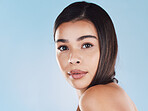 Portrait of one beautiful young hispanic woman with healthy skin and sleek hair posing against a blue studio background. Mixed race model with flawless complexion and natural beauty