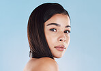 Portrait of one beautiful young hispanic woman with healthy skin and sleek hair posing against a blue studio background. Mixed race model with flawless complexion and natural beauty