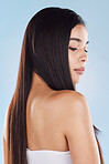 One beautiful young hispanic woman with healthy skin and sleek long hair looking over shoulder while posing against a blue studio background. Mixed race model with flawless complexion and natural beauty