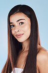 Portrait of one beautiful young hispanic woman with healthy skin and sleek long hair smiling against a blue studio background. Happy mixed race model with flawless complexion and natural beauty