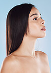 One beautiful young hispanic woman with healthy skin and sleek hair posing against a blue studio background. Mixed race model with flawless complexion and natural beauty