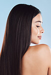 One beautiful young hispanic woman with healthy skin and sleek long hair looking over shoulder while posing against a blue studio background. Mixed race model with flawless complexion and natural beauty