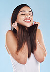 One beautiful young hispanic woman touching her sleek, silky and healthy long hair while smiling against a blue studio background. Confident and happy mixed race model with flawless complexion and natural beauty