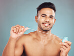 Portrait of one smiling young indian man flossing his teeth against a blue studio background. Handsome guy grooming and cleaning his mouth for better oral and dental hygiene. Floss daily to prevent tooth decay and gum disease