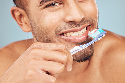 Buy stock photo Man, brushing teeth and health in studio portrait for self care, hygiene or dental wellness by blue background. Person, model and toothbrush for grooming, oral and closeup to clean mouth in Colombia