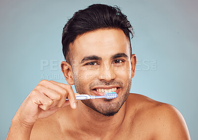 Buy stock photo Man, brushing teeth and happy in studio portrait for self care, hygiene or oral wellness by blue background. Person, model and toothbrush for grooming, smile and cleaning mouth for health in Colombia