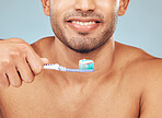 Closeup of one mixed race man brushing his teeth against a blue studio background. Guy grooming and cleaning his mouth for better oral and dental hygiene. Brush twice daily to prevent tooth decay and gum disease