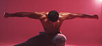 One strong indian man stretching arms while crouching against a red studio background. Fierce muscular and topless man with toned body looking ready to fight or demonstrate powerful martial arts moves