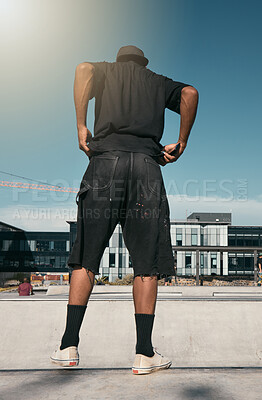 Buy stock photo Skate clothes, urban fashion and man with emo, goth or gen z contemporary street style at fitness skate park for training. Blue sky lens flare, concrete building and back view of stylish black person