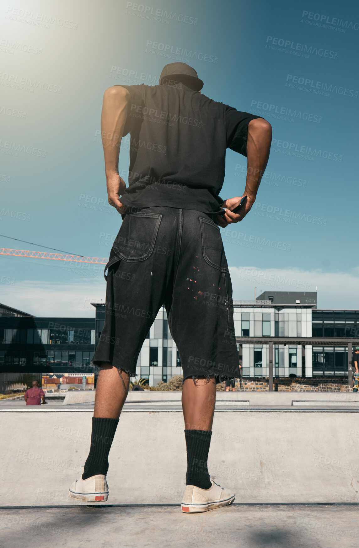 Buy stock photo Skate clothes, urban fashion and man with emo, goth or gen z contemporary street style at fitness skate park for training. Blue sky lens flare, concrete building and back view of stylish black person