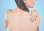 Back, woman and water splash for skincare, clean and hygiene against blue studio background. Young female, girl and liquid drops for washing, body care or natural beauty for wellness, shower or relax