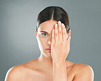 Face, cover and portrait of a woman with a hand on eye isolated on a grey studio background. Skincare, beauty and serious model hiding eyes for dermatology, skin problem and cosmetics on a backdrop