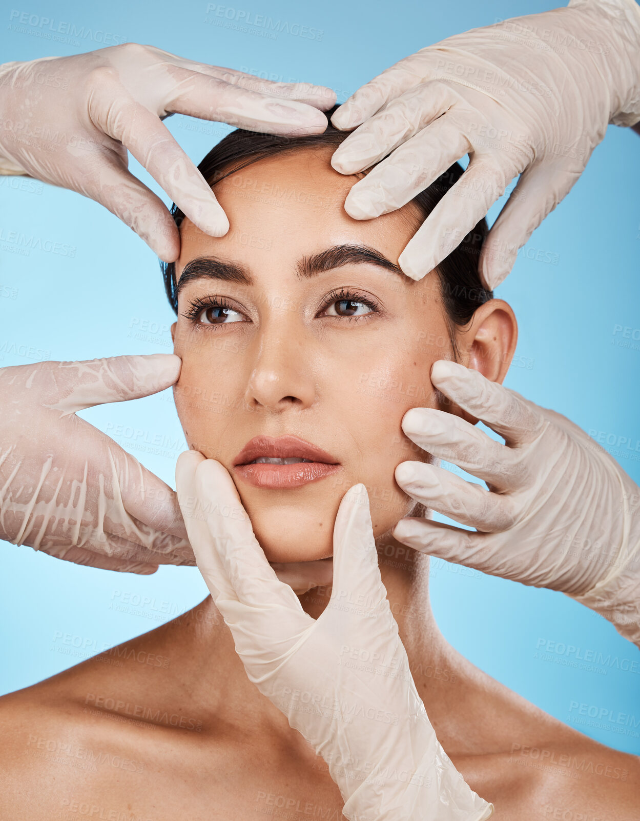 Buy stock photo Plastic surgery, check and hands on the face of a woman isolated on a blue background in a studio. Feeling, skincare and doctors touching a model for a filler, cosmetics or dermatology consultation