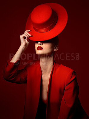 Buy stock photo Hat, fashion and a model woman on a red background in studio for elegant or trendy style. Aesthetic, art and beauty with a confident young female person posing in an edgy, classy or unique suit