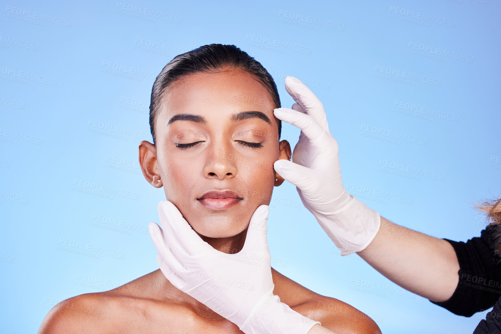 Buy stock photo Beauty, doctor and face of Indian woman for plastic surgery, cosmetics and facial treatment in studio. Dermatology, consulting and hands person for anti aging, collagen and skincare on blue background