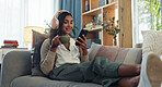 Headphones, indian woman and cellphone for music in home, listen and song in living room. Coffee, relax and online audio streaming or podcast for break, chai tea and happy female person on sofa 