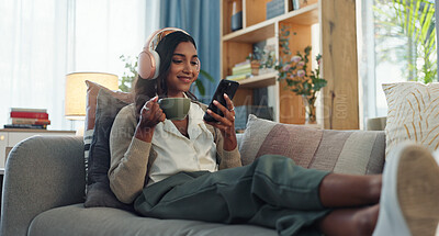 Buy stock photo Headphones, indian woman and cellphone for music in home, listen and song in living room. Coffee, relax and online audio streaming or podcast for break, chai tea and happy female person on sofa 