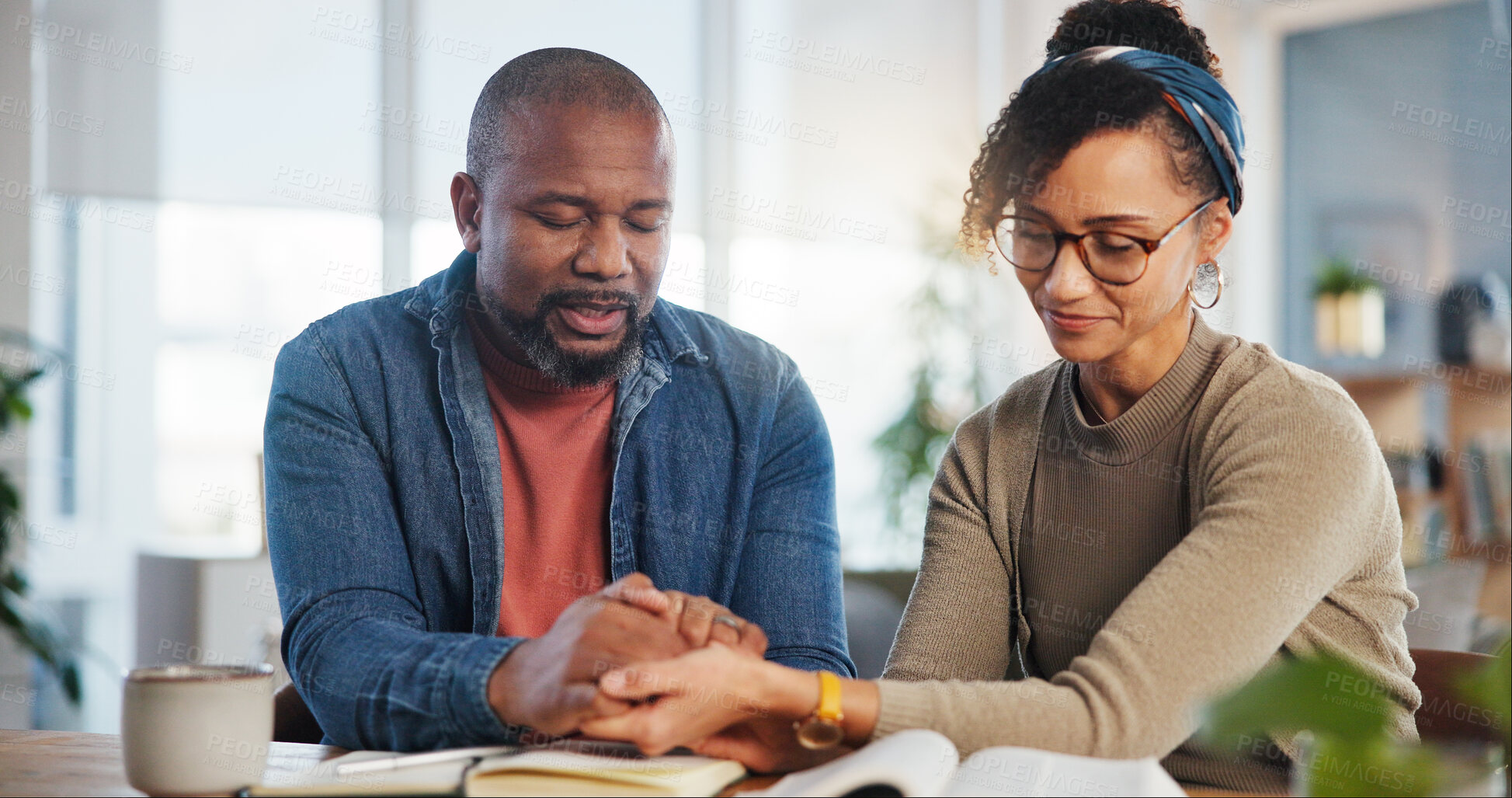 Buy stock photo Couple, holding hands and praying with bible as Christian for spiritual guidance, belief and knowledge. Relationship, home and religion with scripture on holy book for worship, gratitude and faith