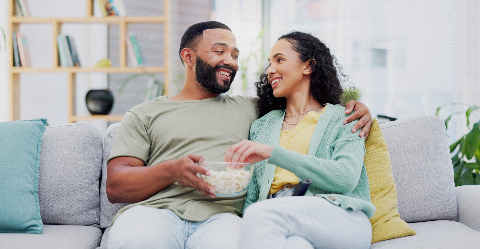 Buy stock photo Couple, popcorn and happy on sofa in home for watching tv with hug, care or relax together in living room. Man, woman and connection with smile, snack and eating on couch for movie date at apartment