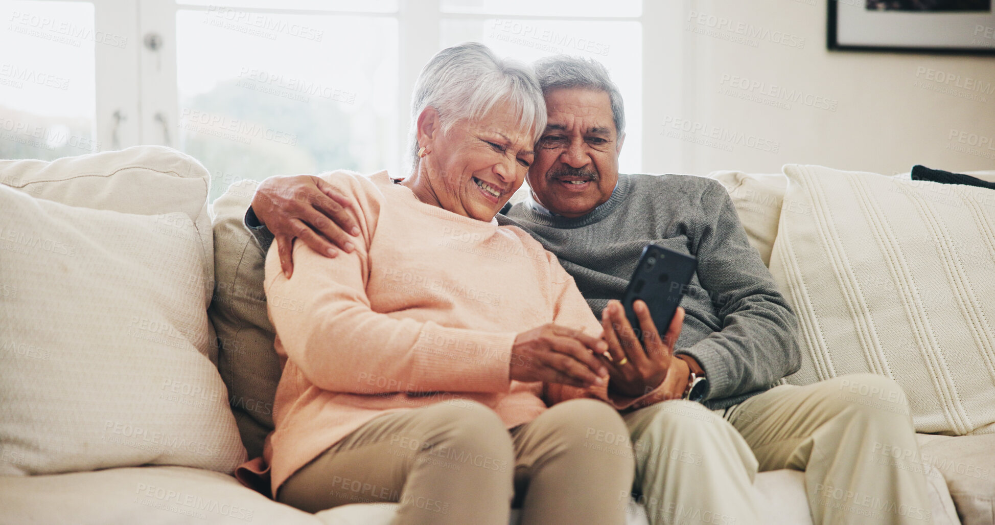 Buy stock photo Senior couple, smartphone and happy on sofa with hug, reading and notification with funny story in home. Woman, man and phone in retirement, relax and embrace with comic memory on mobile app in house