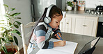 Girl, home and writing with tablet for online education in kitchen with homework and elearning. Kid, counter and notebook with headphones on virtual class or tutorial for child development and growth