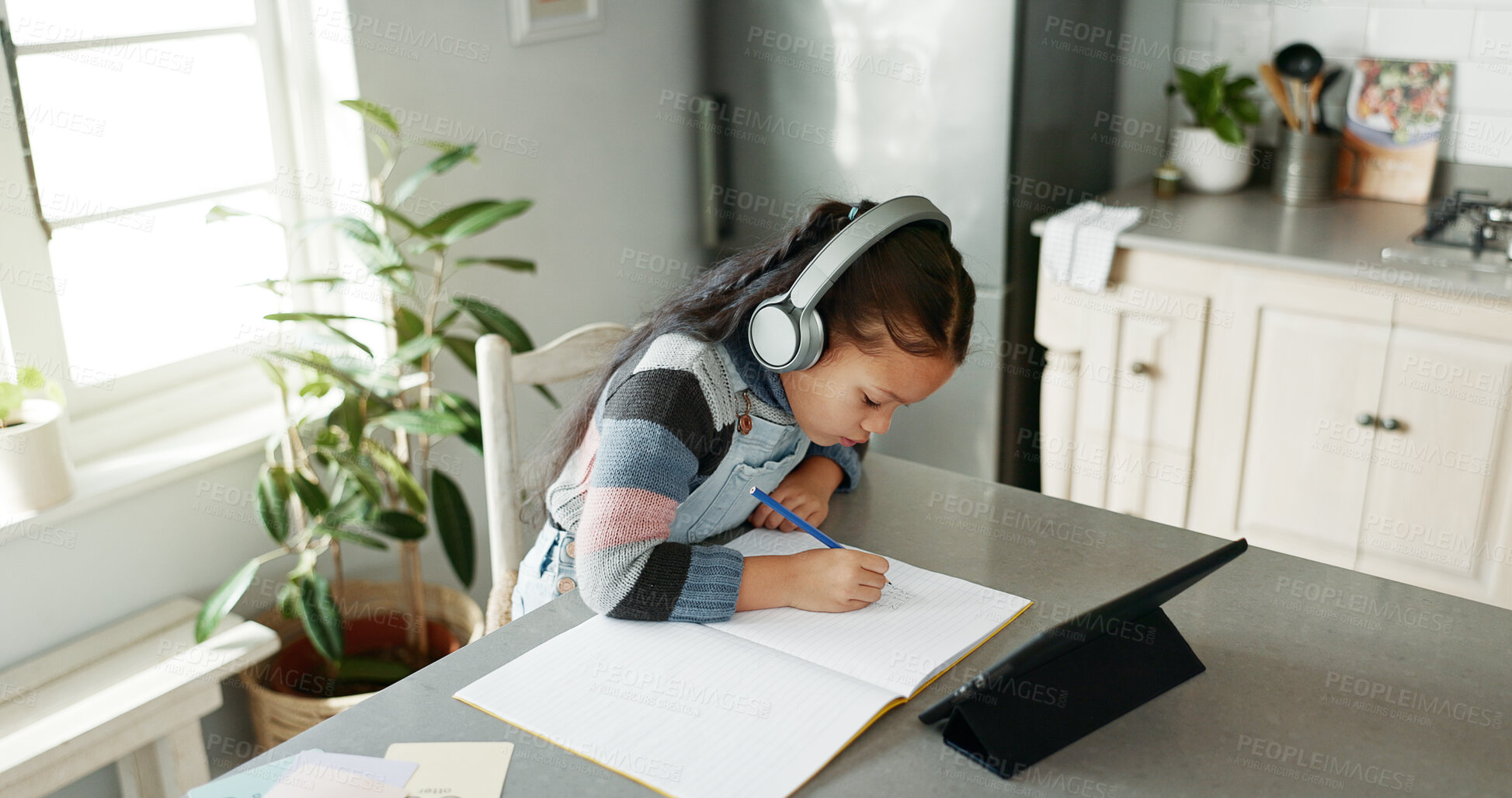 Buy stock photo Kitchen, girl and homework with tablet for education, elearning and connection for online class. Child, studying and cognitive development with writing for learner, knowledge and headphones at home