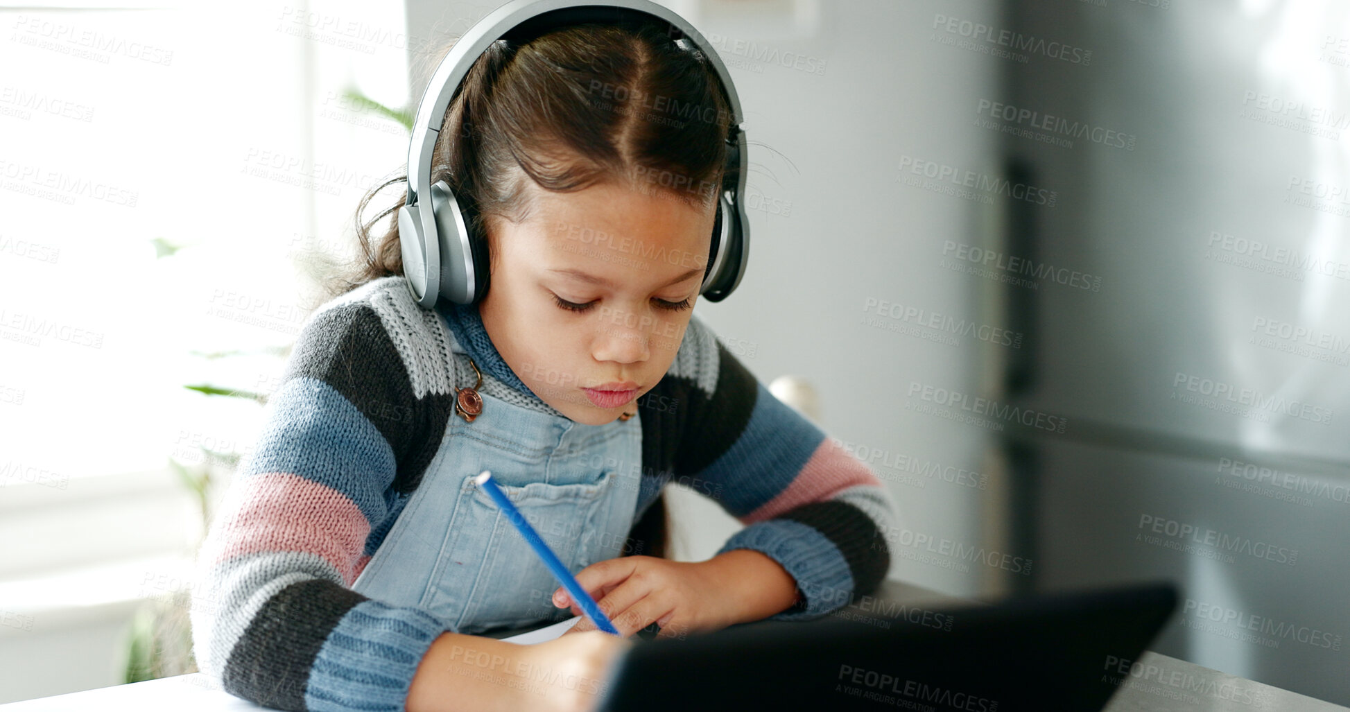 Buy stock photo Home, girl and homework with tablet for education, elearning and connection for online class. Child, studying and cognitive development with writing for learner, knowledge and headphones in kitchen