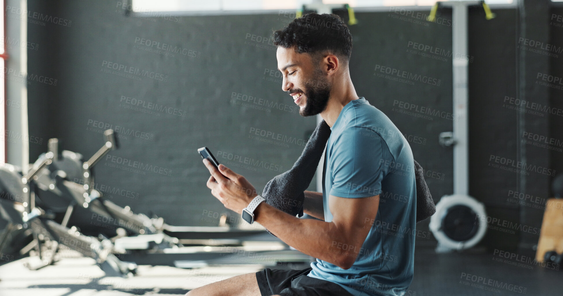 Buy stock photo Man, gym and happy with smartphone on rower machine for social media post and interaction. Male person, sports center and profile for fitness with smile or laugh on internet for fun videos or memes