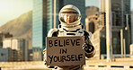 Person, astronaut and outdoor with note on poster in city for career inspiration, motivation and courage. Portrait, employee and outside with card or sign board on spacesuit for proud message 