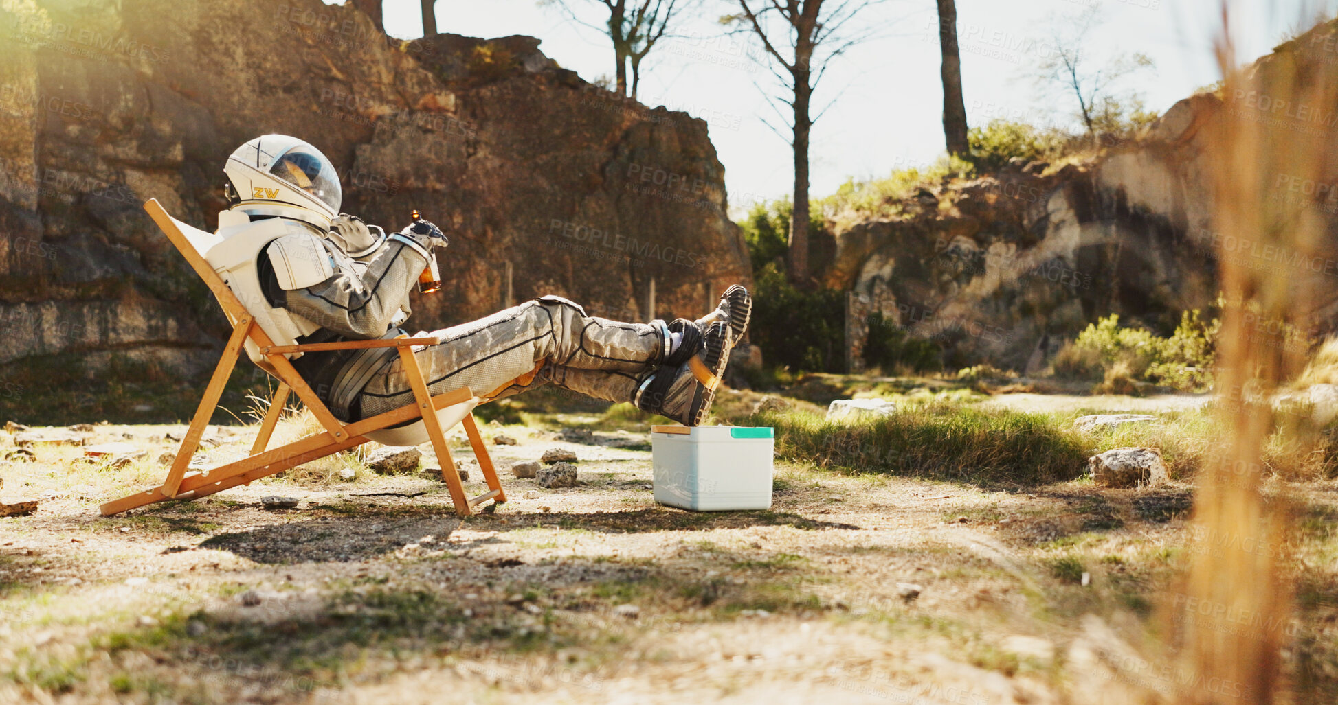 Buy stock photo Relax, nature and astronaut on camping trip for vacation, holiday or getaway in Norway. Person, cooler box and space pilot drinking beer and resting outdoor in woods for weekend chill on break.