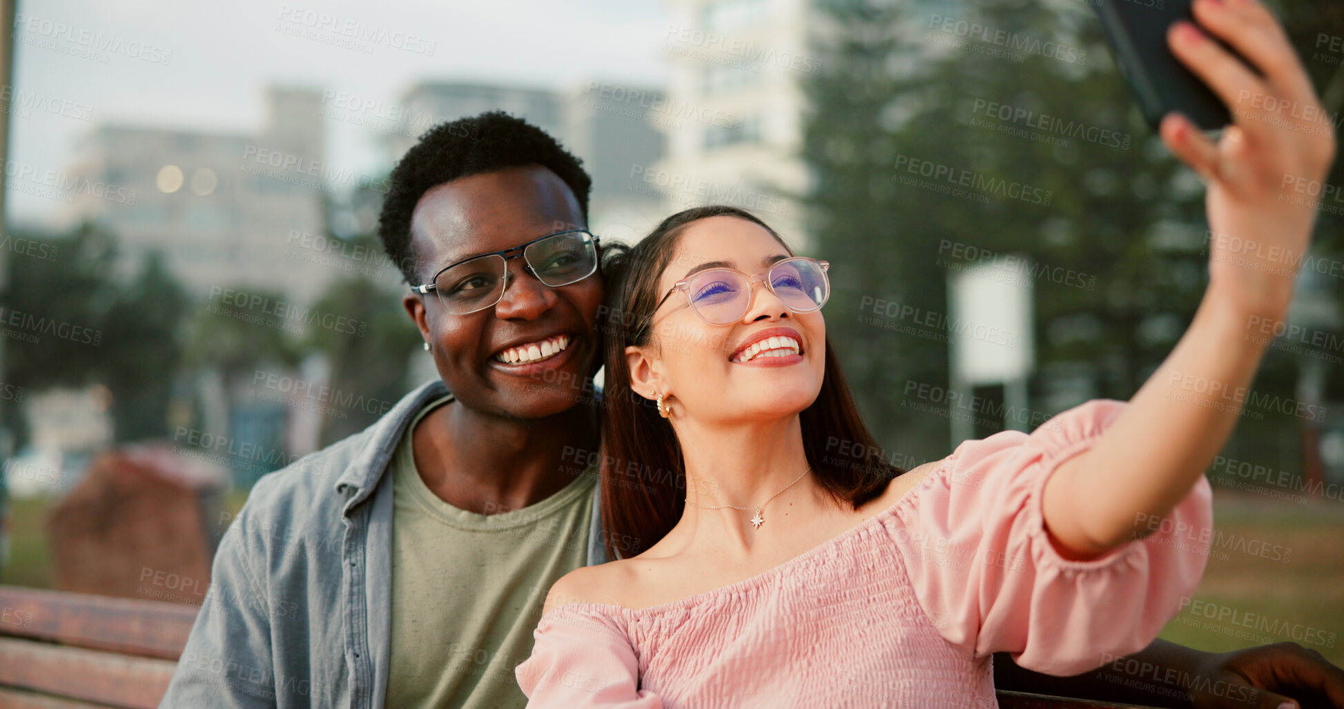 Buy stock photo Smile, selfie and couple on bench in park with fun memory, social media post and interracial relationship. Love, photography and happy man with woman on romantic date with outdoor bonding together