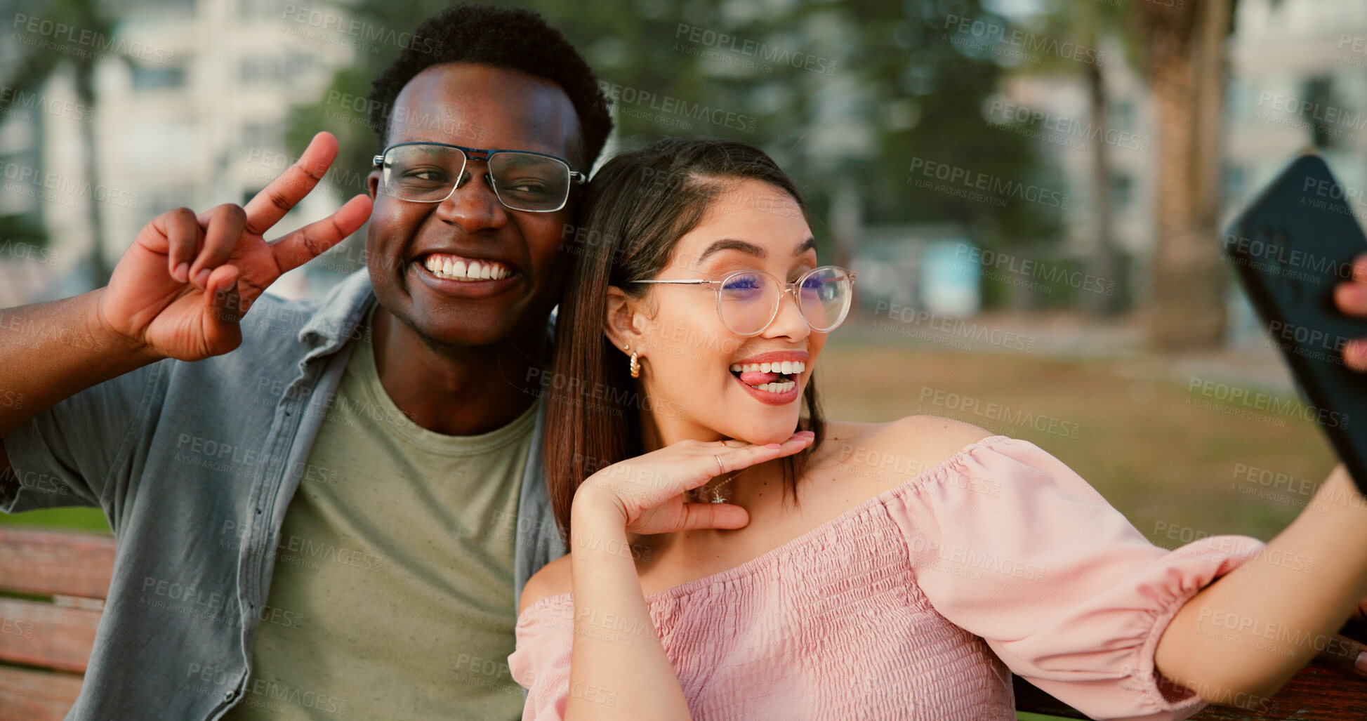 Buy stock photo Fun, selfie and couple on bench in park with goofy memory, social media post and interracial relationship. Love, photography and happy man with woman on romantic date with outdoor bonding together