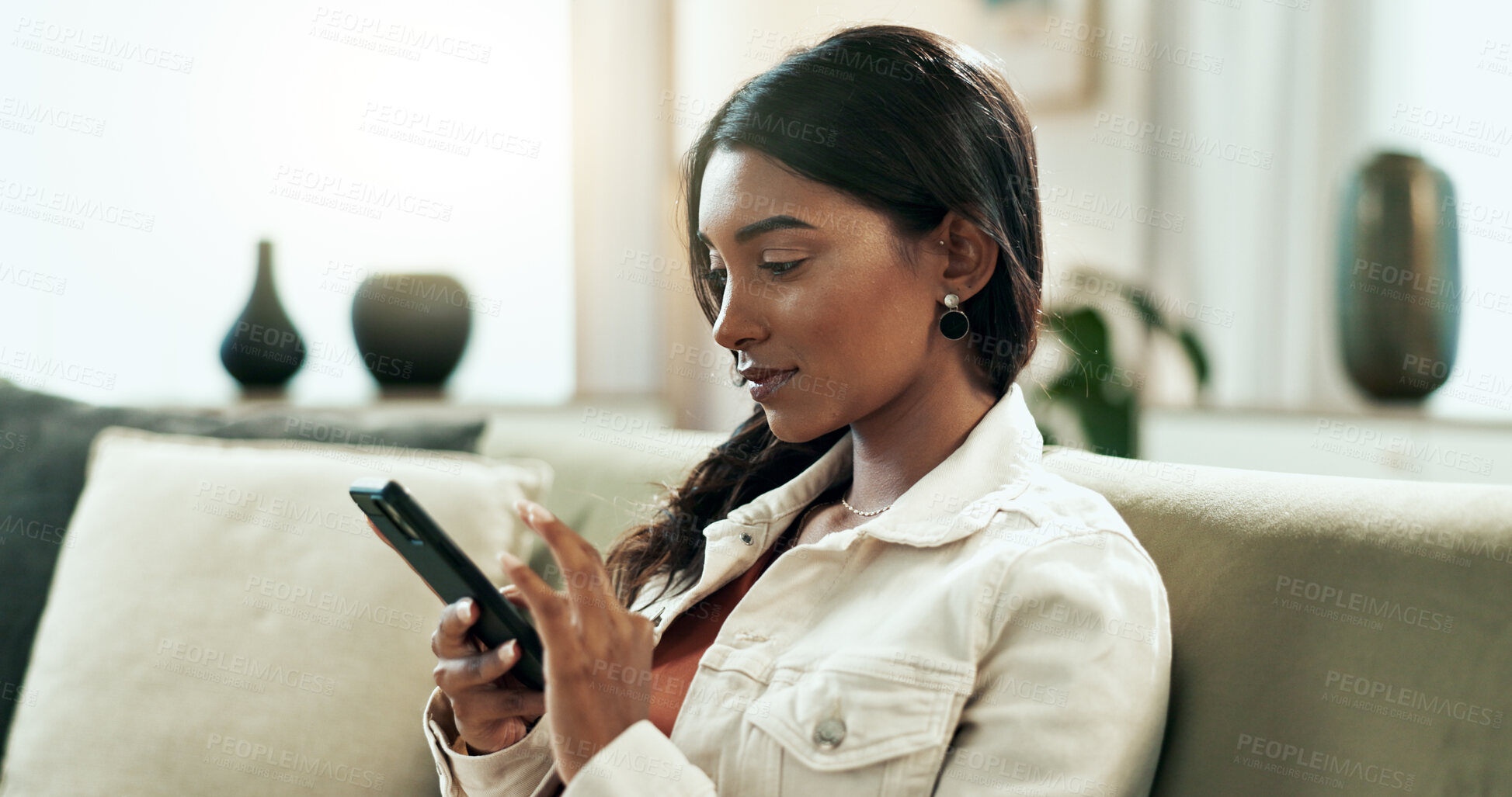 Buy stock photo Phone, relax and social media with Indian woman on sofa in living room of home for communication. App, connectivity and networking with happy person in apartment for text message on weekend morning