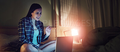 Buy stock photo Shot of a young woman video chatting on a laptop at night while sitting on her bed in her bedroom