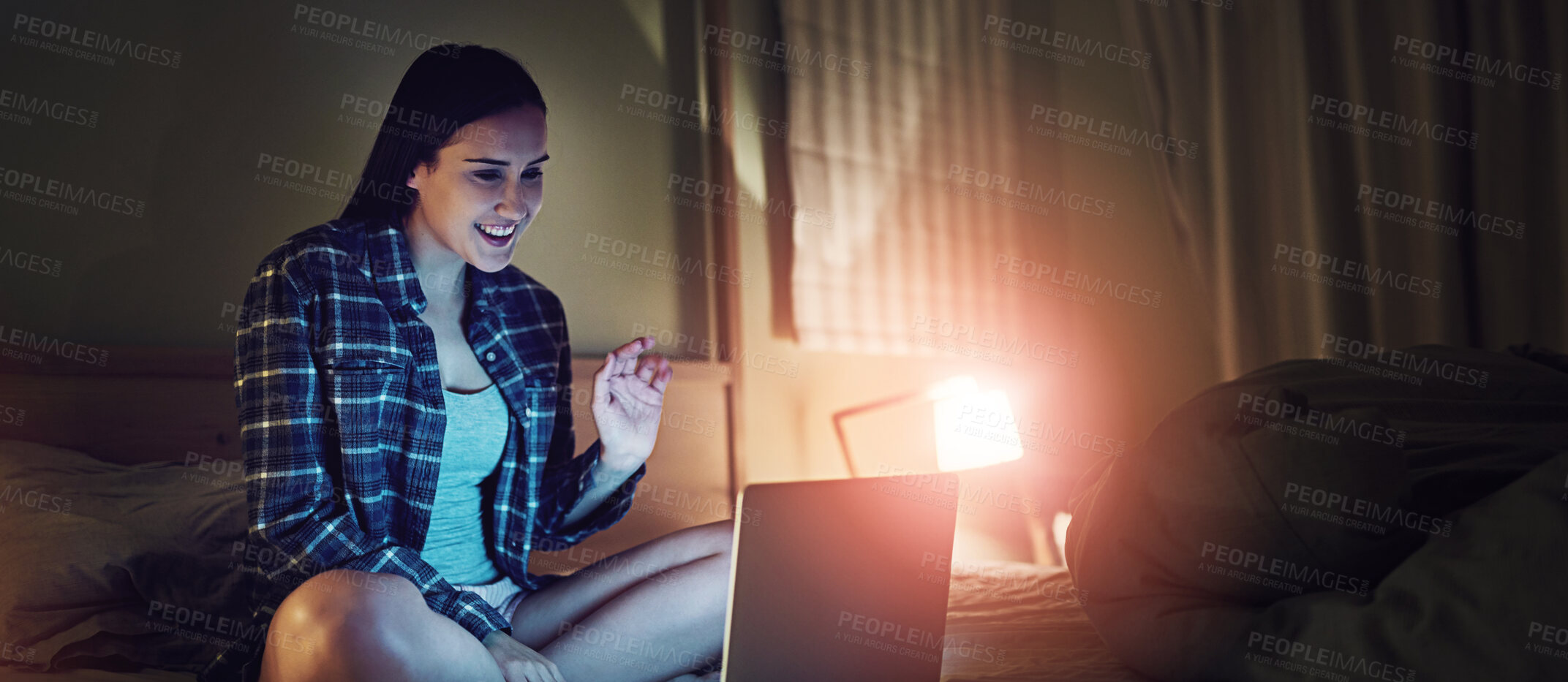 Buy stock photo Shot of a young woman video chatting on a laptop at night while sitting on her bed in her bedroom