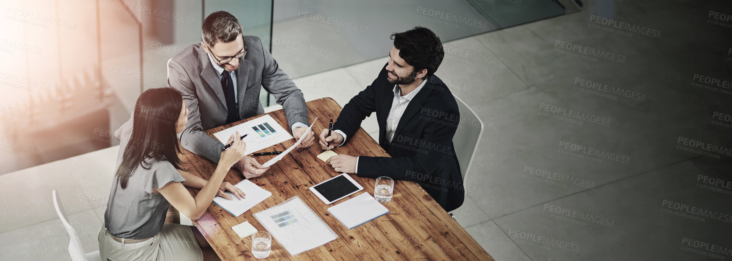 Buy stock photo Shot of three colleagues sitting around a meeting tablet in the office